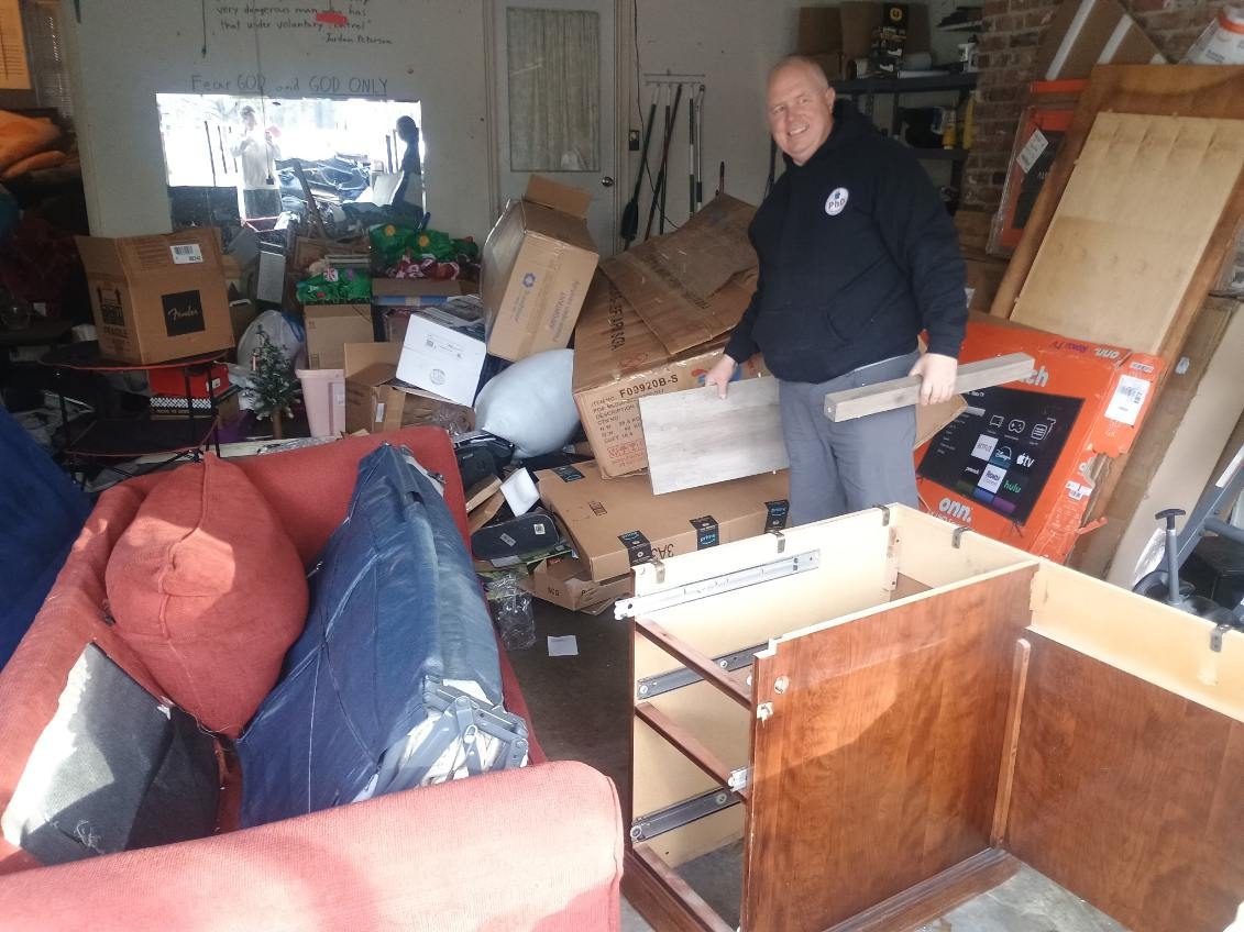 A PhD Junk Removal crew member in a garage packed with boxes, a sofa and a dismantled dresser